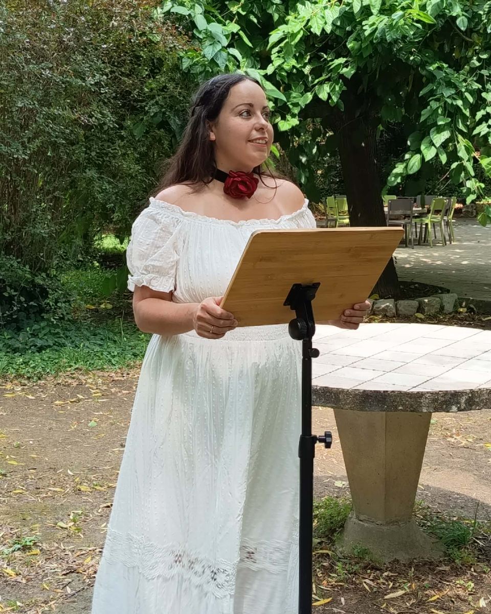Marjorie, prêtresse païenne, célébrant au pupitre en robe blanche et rose rouge au cou